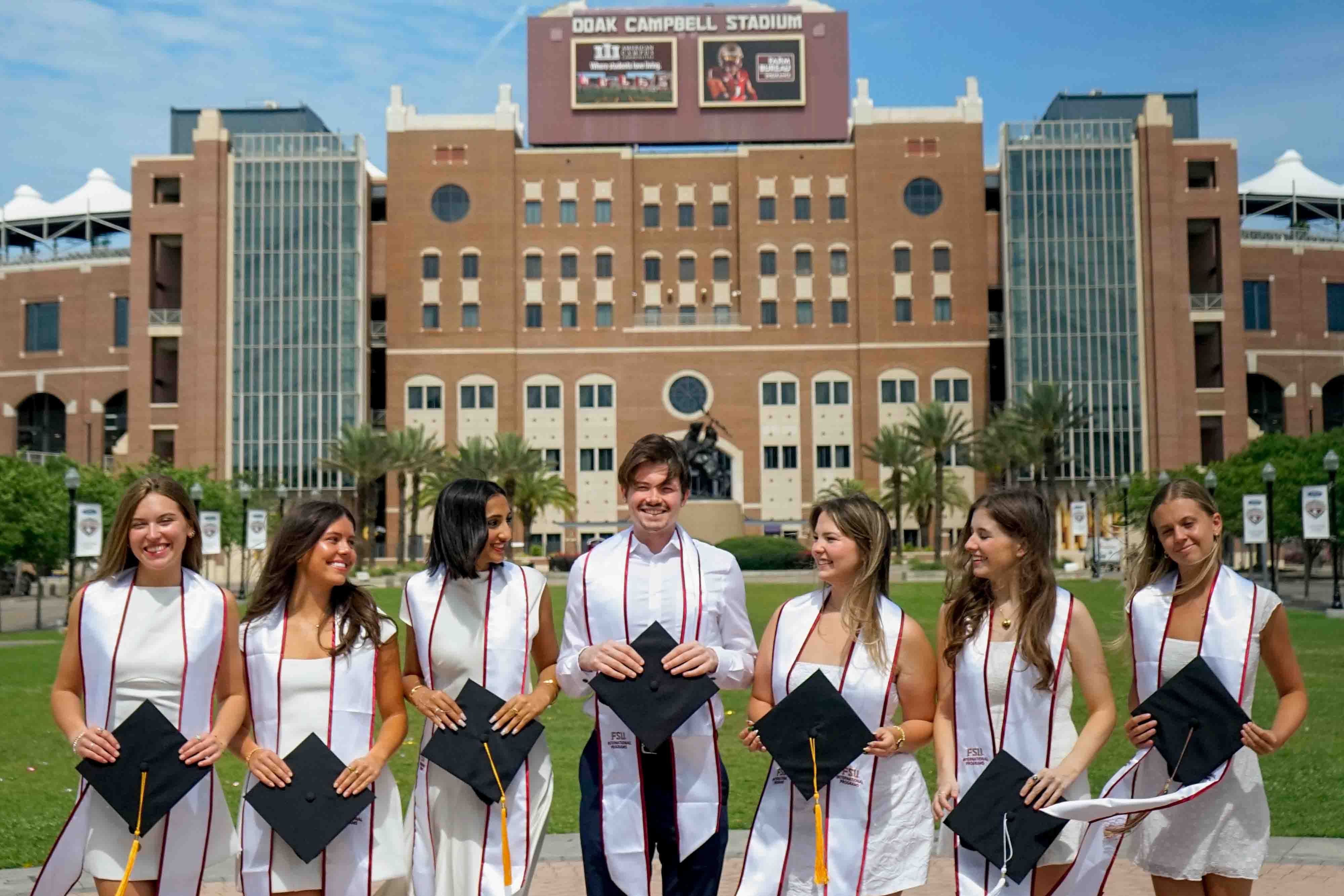 FSU IP students in graduation outfits holding their caps and wearing International Programs stoles.